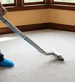 Steam carpet cleaning technician using a hot-water extraction wand on a residential carpet, wearing blue protective shoe covers Tempe, AZ.