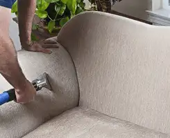 Professional upholstery cleaner deep-cleaning a fabric sofa with a handheld extraction tool and hose in Tempe, AZ.